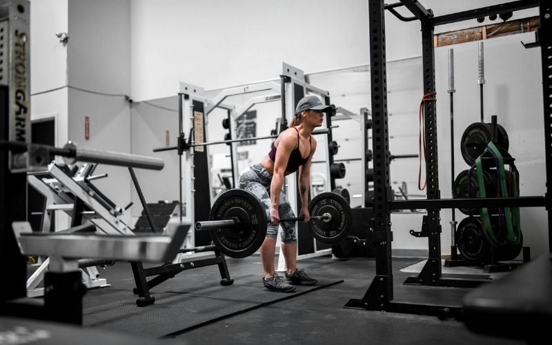 Woman in leggings, sports bra, and baseball cap doing deadlifts.