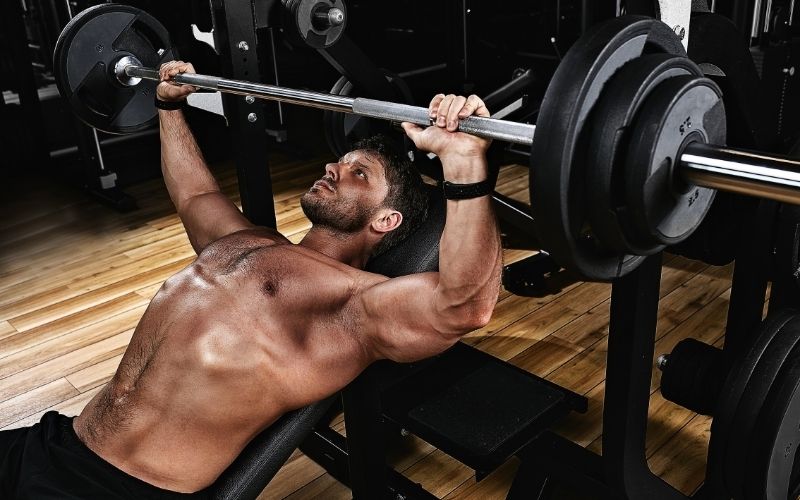 Shirtless man doing incline bench press.
