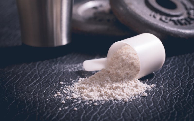 Protein scoop on black leather background in front of weights and silver cup.