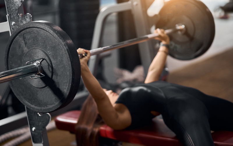 Woman doing barbell bench press in gym