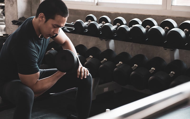 Brunette man leaning over doing a dumbbell single arm bicep curl.