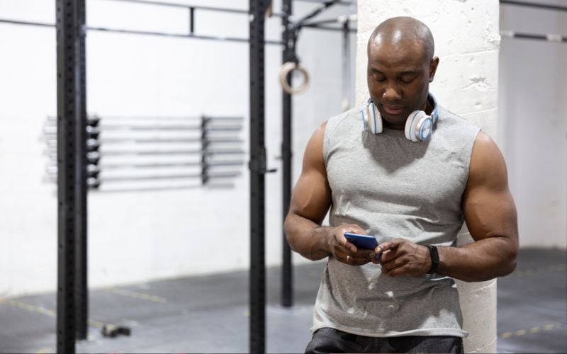 African American man tracking weightlifting progress on his phone. 