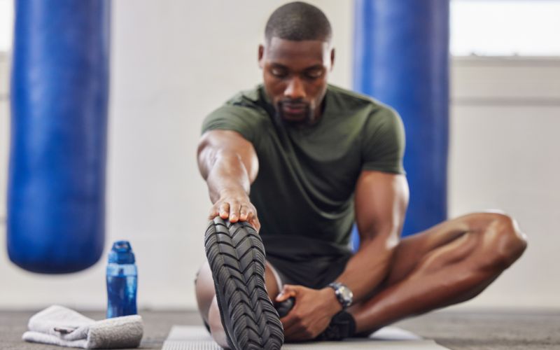 Fit man doing a lower body stretch on the floor in the gym.