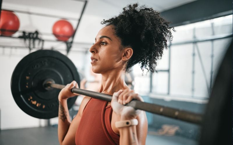 Side profile shot of a woman doing barbell shoulder press.