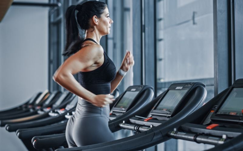 Lean female running on the treadmill in the gym.