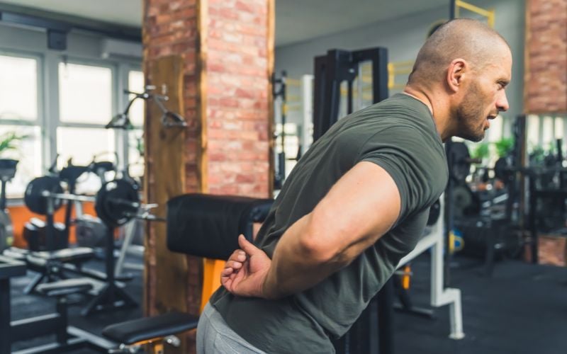 Muscular man with back pain at the gym gym.