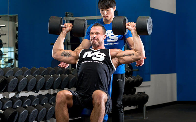 M&S Athlete Performing Dumbbell Shoulder Press With a Spotter
