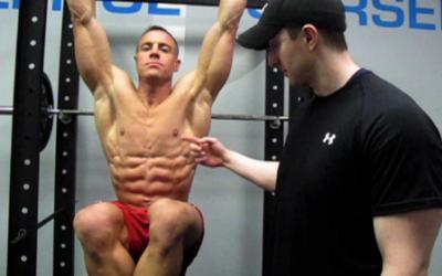 Shirtless man doing hanging knee raises in the gym