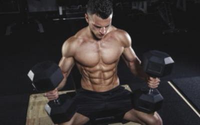 Ripped man sitting with 2 dumbbells in the gym