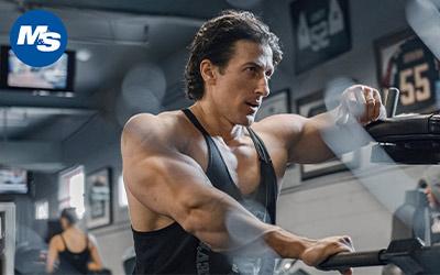 Side profile shot of a muscular bodybuilder wearing a tank top in the gym