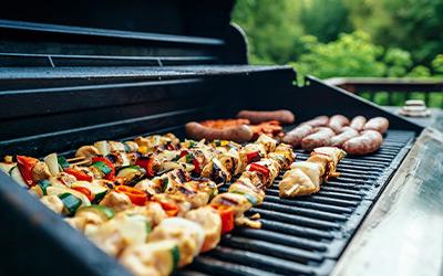 Chicken and vegetable kabobs with sausage and burger patties on the grill outside.
