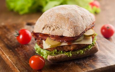 Close up of turkey sandwich with lettuce, cheese, and pickles surrounded by cherry tomatoes.