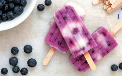 Healthy fruit and yogurt popsicles with a side of blueberries on the countertop.