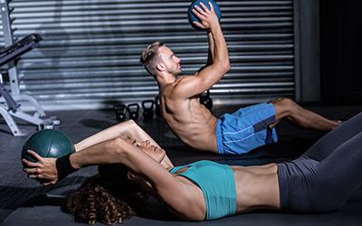 Lean man and woman using medicine balls to do ab workouts on the gym floor.