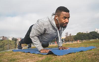 Man in a push up position working out outside while listening to music.