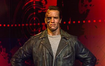 Close up of Arnold Schwarzenegger wearing a leather jacket against a red and black background.