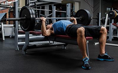 Strong man doing barbell chest presses on a flat bench.