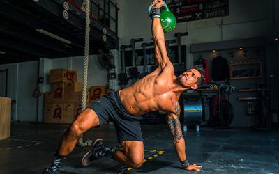 Muscular man holding a kettlebell while doing a Turkish Get-Up.