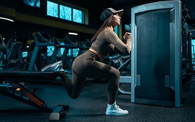 Fit woman doing single leg split squats on workout bench in the gym.