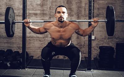 Frontal shot of a strong muscular man doing a barbell back squat.