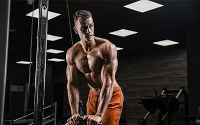 Muscular man holding cable attachment while doing tricep pushdowns. 