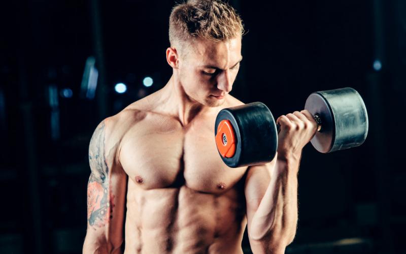 Shirtless muscular man doing single arm bicep curls.