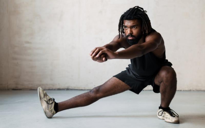 Man in black shorts and black tank top doing lateral lunges.