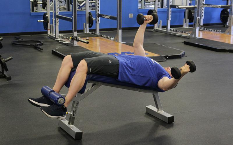 Fit man doing an alternating dumbbell fly on an incline bench in the gym.
