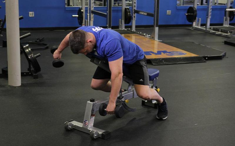 Fit man doing alternating incline rear delt flys in the gym.