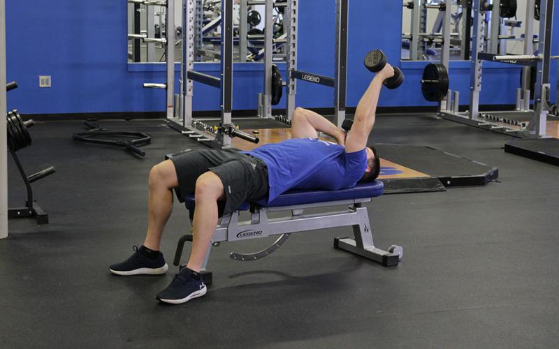 Fit man doing an alternating lying dumbbell extension in the gym.