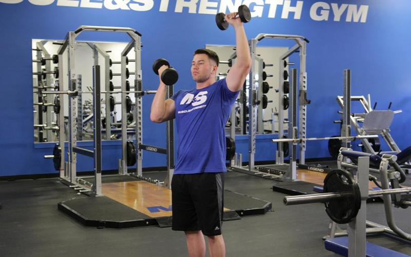 Fit man doing an alternating standing arnold press in the gym.