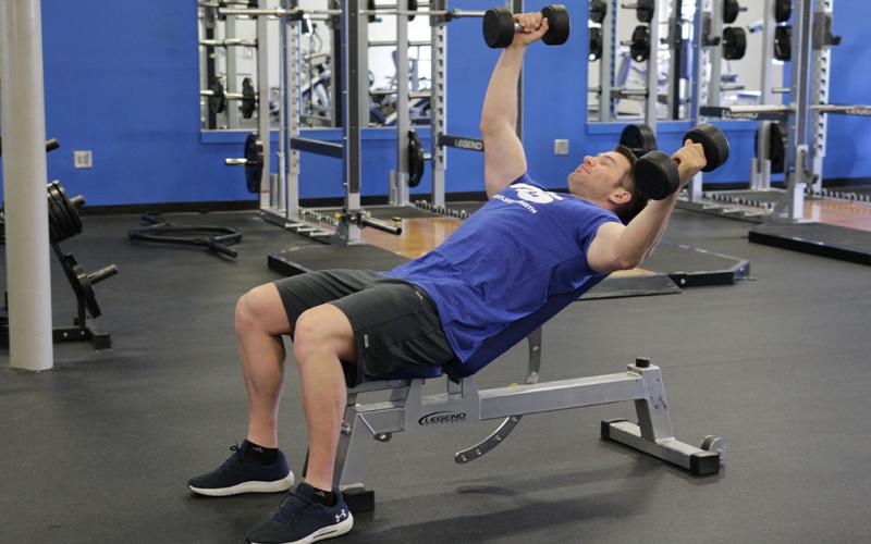 Fit man doing an alternating incline dumbbell fly in the gym.