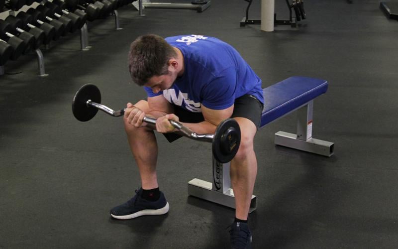 Fit man doing a barbell concentration curl in the gym.