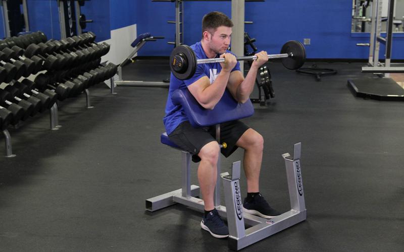 Fit man doing a barbell preacher curl in the gym.