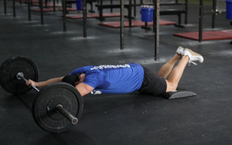 Fit man doing a barbell abdominal rollout in the gym.