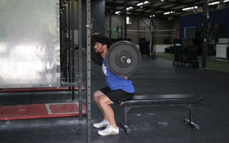 Fit man doing a barbell box squat in the gym.