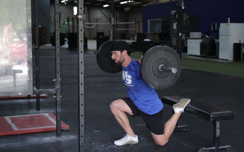 Fit man doing a Barbell Bulgarian Split Squat in the gym.
