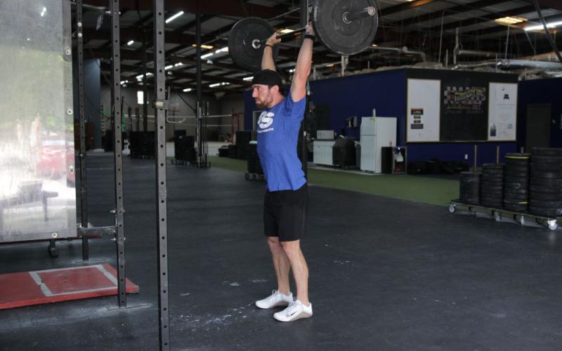 Fit man doing a barbell clean and press in the gym.