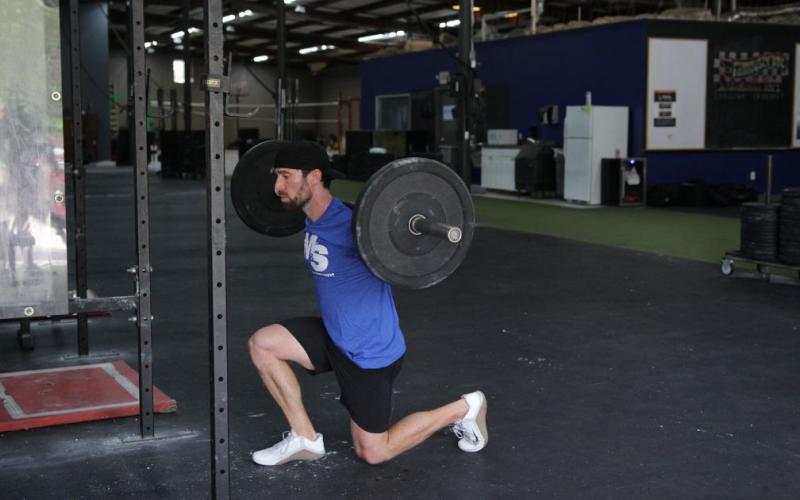 Fit man doing barbell lunges in the gym.