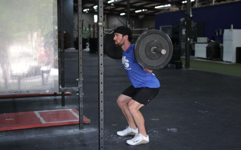 Fit man doing a barbell quarter squat in the gym.