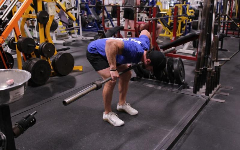 Fit man doing a barbell rear delt row in the gym.