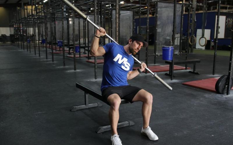 Fit man doing Barbell Side Bends in the gym.