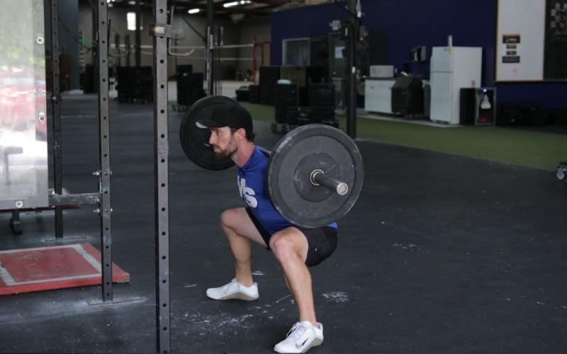 Fit man doing barbell sumo squats in the gym.