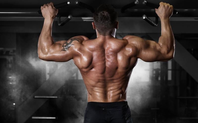 Bodybuilder doing wide grip pull up in dark gym