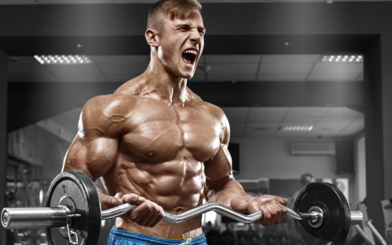 Shirtless, muscular man doing ez-bar bicep curls.