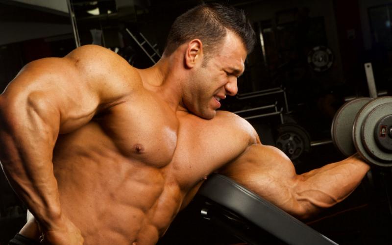 Shirtless muscular man dong single arm bicep curls.