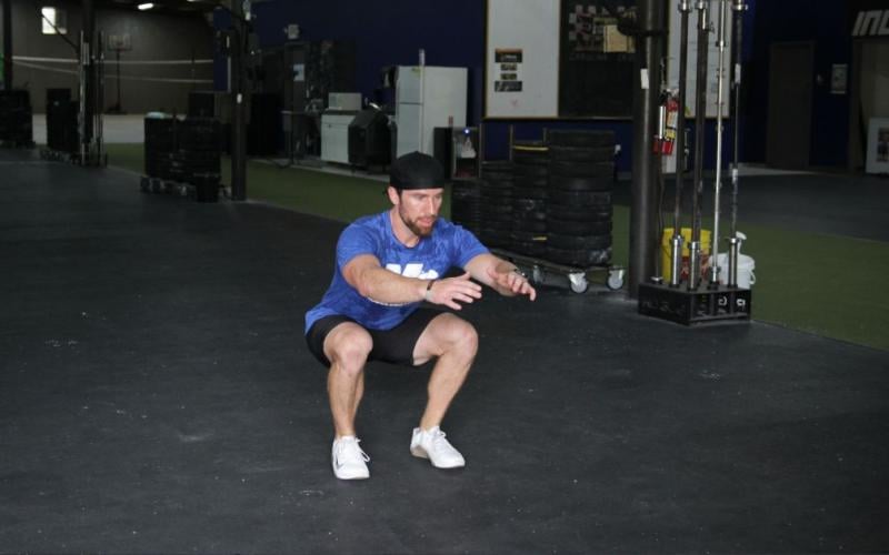 Fit man doing a bodyweight squat jump in the gym.