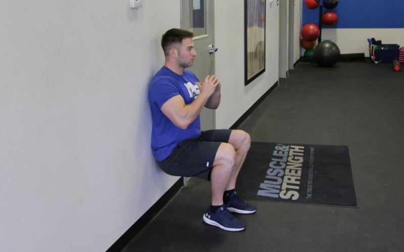 Fit man doing a Bodyweight Wall Squat in the gym.