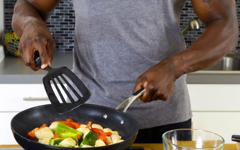 Muscle & Strength athlete in grey M&S t-shit cooking chicken and peppers on the stove.