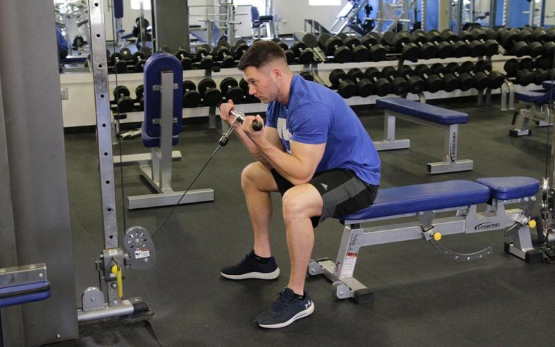 Fit man doing a cable concentration curl in the gym.
